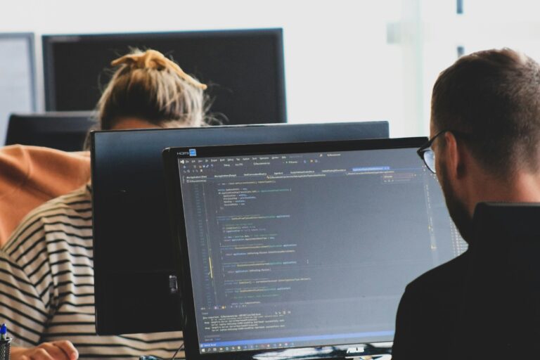 Two software developers working on code at monitors in a bright engineering workspace