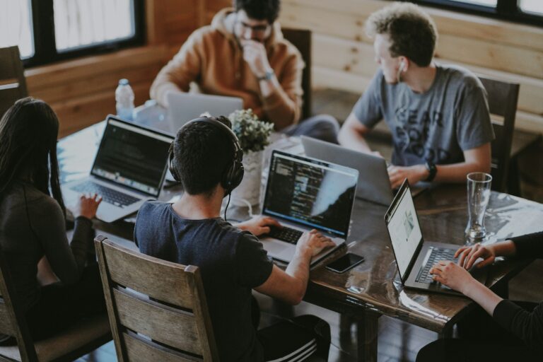 A distributed software team collaborating around a shared table, working on laptops with code on screen
